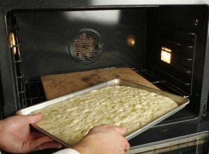 Placing the pan on the stone in the oven during the focaccia step-by-step process.